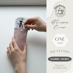 May include: A pink glasses case with white polka dots is being opened to reveal a pair of black glasses. The case is made of fabric and has a button closure. The text "Glasses Case" and "ONE SIZE" are visible.