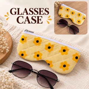 Peut inclure: Un étui à lunettes jaune matelassé orné d'un motif répétitif de fleurs orange à cœur noir, doté d'une fermeture éclair blanche et d'une forme profilée, accompagné d'une paire de lunettes de soleil teintées à monture métallique fine.