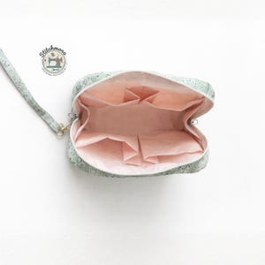 May include: Open view of a light green patterned clutch with a wrist strap. The interior is a soft pink with multiple pockets. The clutch has a zipper closure and gold-colored hardware. The logo "Stitchmora Sewing Patterns" is visible.