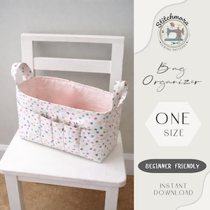 May include: A fabric bag organiser with a white exterior patterned with colourful stars. The interior is lined with pink fabric. The bag has handles and several exterior pockets. Text on the image reads "Bag Organiser" and "One Size".