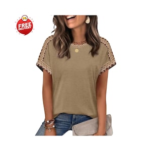 May include: A short-sleeved, tan-colored shirt with embroidered detailing on the shoulders and sleeves. The shirt has a round neckline and is paired with blue jeans. The image also includes a free delivery icon.