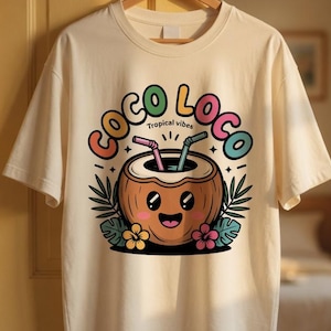 May include: Cream-colored t-shirt with a colorful "Coco Loco" graphic featuring a smiling coconut drink with straws, surrounded by tropical leaves and flowers. The words "Tropical vibes" are also included.