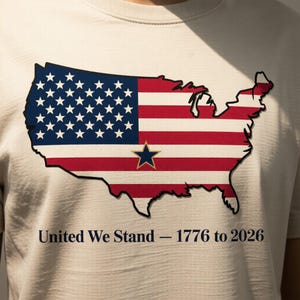 Puede incluir: Una camiseta de color claro con un gráfico del mapa de los Estados Unidos al estilo de la bandera estadounidense. El diseño incluye estrellas azules, rayas rojas y blancas y una estrella dorada. El texto "United We Stand - 1776 to 2026" está impreso debajo.