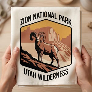 Może przedstawiać: Kremowy ręcznik kuchenny z grafiką owcy gruborogiej na pustynnym krajobrazie. Tekst "ZION NATIONAL PARK UTAH WILDERNESS" jest wydrukowany na czarno. Projekt ma kształt sześciokąta.
