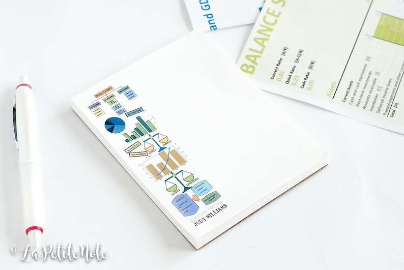 May include: White notepad with colorful business charts and graphs. A white pen with red accents is on the left. The notepad has the name "JUDY WILLIAMS" printed on it. A document with the words "BALANCE SHEET" is in the background.