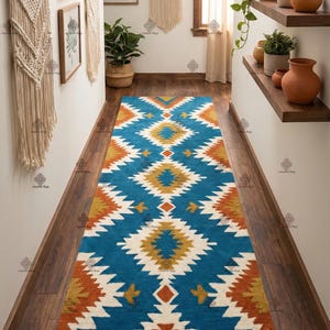May include: A long, rectangular rug with a geometric pattern in shades of blue, orange, yellow, and white. The rug is placed on a dark wood floor in a hallway. The rug's design features diamond and zig-zag shapes.