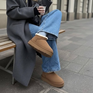 Puede incluir: Botines marrones con suela de plataforma y ribete interior blanco y esponjoso. Las botas están hechas de material similar al ante y tienen una suela exterior resistente. Las botas se usan con jeans azules.