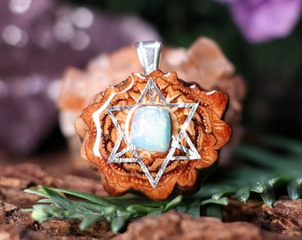 May include: A silver pendant featuring a six-pointed star with a light blue opal gemstone in the center. The star is carved into a piece of wood with a brown and orange color.