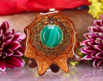 May include: A handcrafted pendant featuring a vibrant green malachite stone set in a detailed, wooden, starburst-shaped frame. The pendant has a silver bail and is displayed against a blurred floral background.