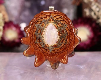 Può includere: Un ciondolo fatto a mano con un motivo a stella e una pietra centrale a forma di goccia di colore chiaro. Il ciondolo è realizzato in legno con un motivo intagliato dettagliato e un'ansa color argento. La combinazione di colori è marrone caldo e crema.