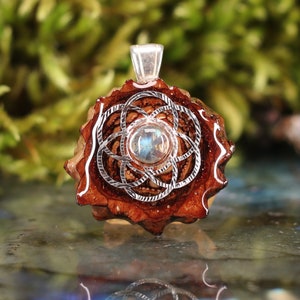 Puede incluir: Un colgante de plata con una piedra preciosa de labradorita engastada en un círculo de madera con un diseño de flor de la vida plateado.