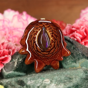 Puede incluir: Un colgante de madera marrón con un patrón de espiral y una piedra preciosa de ópalo en forma de lágrima en el centro.