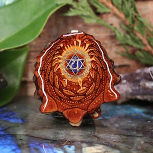 Puede incluir: Un colgante de madera con un diseño geométrico dorado y azul. El colgante tiene forma de flor con una estrella en el centro.