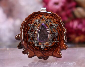 May include: A handcrafted pendant featuring a teardrop-shaped, glittery, purple-blue stone set within a silver-colored Star of David. The pendant is encased in a brown, textured, organic material, possibly wood or resin, with a silver bail.