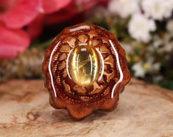 May include: A ring with a yellow gemstone set in a brown resin base with a detailed floral design.