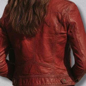 May include: A red leather jacket with a classic design. The jacket features detailed stitching, a button closure at the waist, and a tailored fit. The back view showcases the jacket's structure and texture.