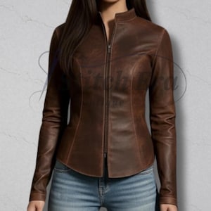May include: A brown leather jacket featuring a stand-up collar and a full-length zip. The jacket has long sleeves and a fitted shape. The leather has a distressed look, giving it a vintage feel. The jacket is worn with blue jeans.