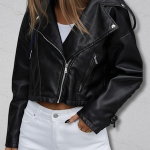 May include: Black cropped faux leather jacket with a silver zip and a notched collar. The jacket has a classic biker style with zipped pockets and a fitted silhouette. The sleeves have a decorative tie detail.