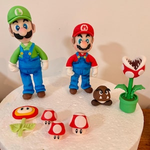 May include: A collection of handmade figurines featuring characters from the Super Mario video game series. Includes Mario and Luigi figures, a Piranha Plant, Goomba, and various mushroom designs. The figurines are brightly colored and made of a soft material.