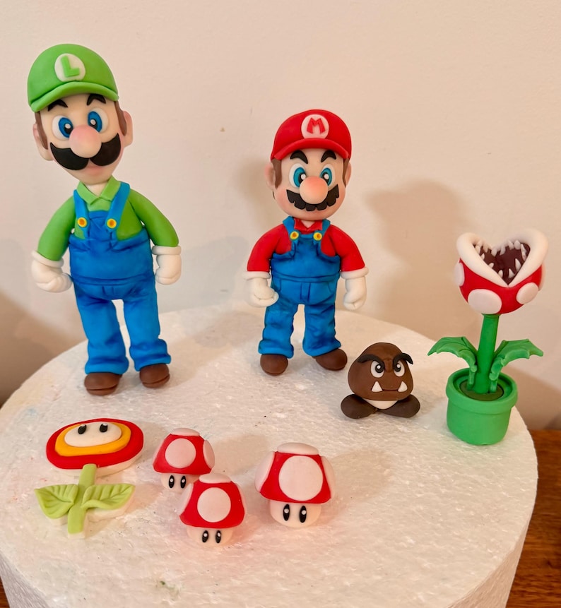 May include: A collection of handmade figurines featuring characters from the Super Mario video game series. Includes Mario and Luigi figures, a Piranha Plant, Goomba, and various mushroom designs. The figurines are brightly colored and made of a soft material.
