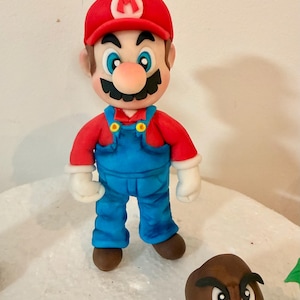 May include: A figurine of Mario, a character from the Super Mario video game series, wearing a red cap with a white "M", a red shirt, and blue overalls. A brown Goomba is also present.