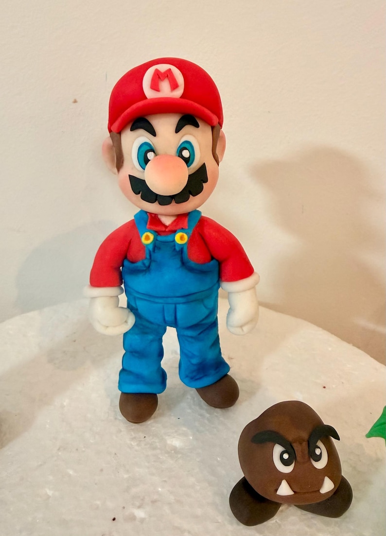 May include: A figurine of Mario, a character from the Super Mario video game series, wearing a red cap with a white "M", a red shirt, and blue overalls. A brown Goomba is also present.