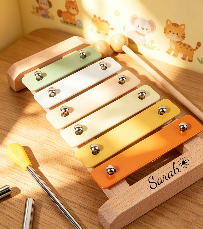 Op de afbeelding: Een houten xylofoon met gekleurde staven in groen, wit, geel en oranje. De xylofoon heeft een houten basis en wordt geleverd met twee hamers. De naam "Sarah" staat op de basis.