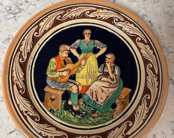 Prato de cerâmica vintage alemão com decoração em relevo representando músicos folclóricos.