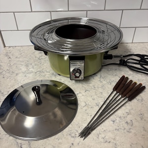 May include: A vintage Panasonic Tempura-Fondue electric pot in olive green with a chrome lid, a circular wire rack, and six metal fondue forks with dark brown wooden handles. The control panel features a black dial and a red indicator light.