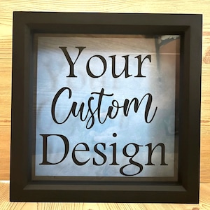 May include: A black square frame with a glass front. The glass has a blue and white cloudy background with the text "Your Custom Design" in black.