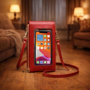 May include: A red crossbody phone bag with a clear front panel displaying a smartphone screen. The bag has a zip closure, gold-coloured hardware, and a matching red strap. The phone screen shows app icons.