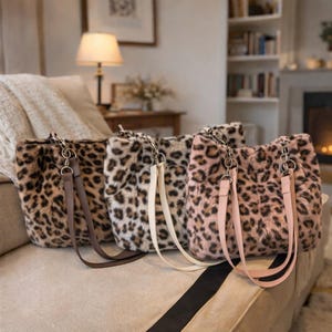 Peut inclure: Quatre sacs fourre-tout en fausse fourrure avec imprimé léopard dans les tons marron, crème et rose. Chaque sac a une poignée en chaîne et une sangle assortie. Les sacs sont exposés sur un canapé beige.