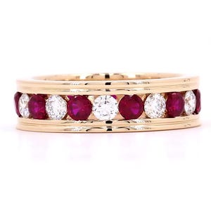 May include: A gold band ring featuring an alternating channel-set row of round-cut deep red rubies and clear white diamonds. The metal band has a polished finish with raised edges framing the stones in a horizontal, symmetrical arrangement.
