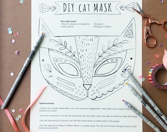 May include: DIY cat mask craft kit with instructions. The black and white cat mask design is on a white sheet of paper. Includes pencils, scissors, and ribbon. The text reads "DIY CAT MASK" and instructions on how to make the mask.