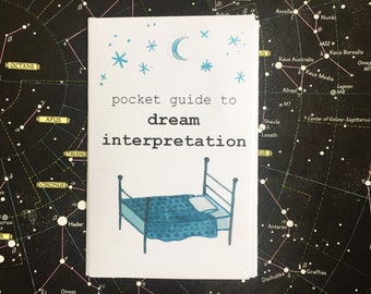 May include: A white pocket guide to dream interpretation with a blue bed illustration, stars, and a crescent moon. The guide is set against a dark background with a star map design.