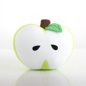 May include: A green plush apple pillow with a white face and black eyes. The apple has a brown stem and a green leaf.