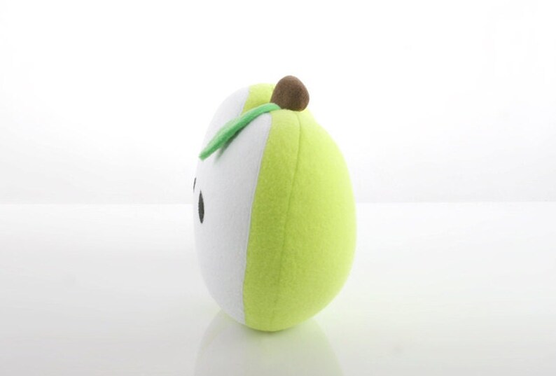 May include: A green and white plush pear with a brown stem and a green leaf. The pear has a simple black face.