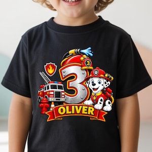 May include: A black t-shirt featuring a graphic of a red fire truck, a Dalmatian puppy in a firefighter helmet, and a large silver number three. The design includes a red banner with the name OLIVER in yellow text and a fire hydrant icon.
