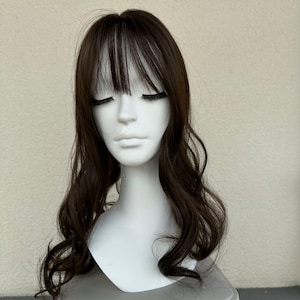 May include: A brown wig with a fringe and long, wavy hair. The wig is displayed on a white mannequin head. The hair has a natural appearance and is styled with a side parting.