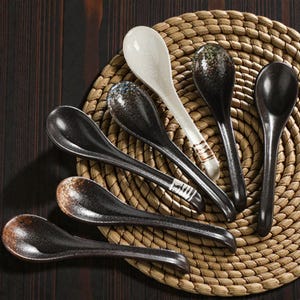 Puede incluir: Una colección de cucharas de cerámica en varios diseños, incluyendo patrones negros, blancos y moteados. Las cucharas están dispuestas sobre un salvamanteles tejido, mostrando sus formas y texturas únicas. Ideales para servir sopas y otros platos.