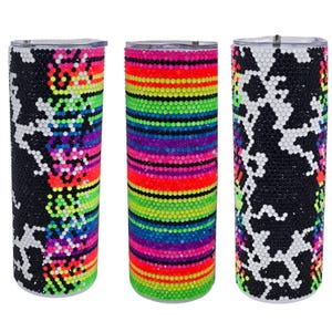 May include: Three cylindrical tumblers covered in small, reflective rhinestones. The left and right tumblers feature a black and white animal print pattern with neon accents. The center tumbler displays horizontal stripes of neon colors.