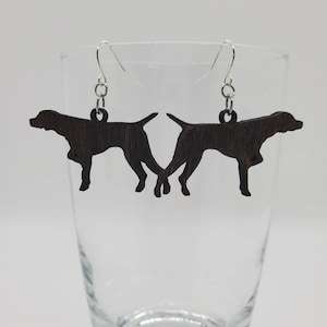 May include: A pair of brown wooden earrings shaped like a silhouette of a dog. The earrings are hanging from silver hooks.