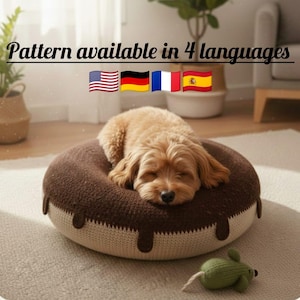 Puede incluir: Un perro pequeño, de color marrón claro, descansa sobre una cama para mascotas con forma de rosquilla. La cama es marrón con ribetes color crema y goteos color chocolate. Un juguete de ratón tejido verde está cerca. El texto dice "Pattern available in 4 languages".