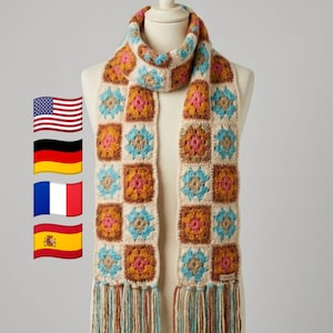 May include: A handmade crochet scarf displayed on a mannequin. The scarf features a repeating square pattern in cream, orange, blue, and brown. The scarf has a fringed edge with matching colors. A cozy and stylish accessory.