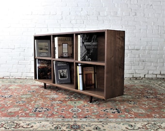 May include: A dark wood bookcase with six shelves, each filled with books. The bookcase has a modern design with a simple, clean look. The bookcase is standing on a patterned rug.