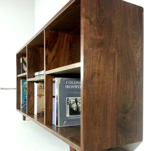 May include: A dark brown wooden bookcase with six shelves, filled with books. The bookcase has a modern design with tapered legs.