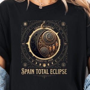 May include: A black t-shirt featuring a gold and dark-toned graphic of a celestial clockwork mechanism. The design includes the text "COSMIC ALIGNMENT," "AUGUST 12, 2026," and "SPAIN TOTAL ECLIPSE" centered within a circular frame of moon phases.