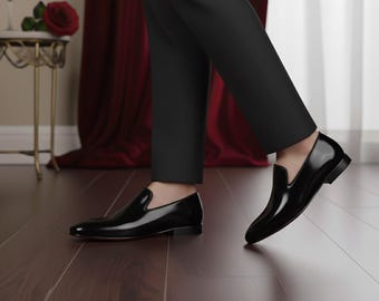May include: A pair of black leather slip-on dress shoes. The shoes have a glossy finish and a low heel. The image shows the shoes from a low angle, highlighting their sleek design. The shoes are part of a formal attire ensemble.