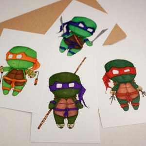 Op de afbeelding: Vier geïllustreerde kaarten met de Teenage Mutant Ninja Turtles. Elke kaart toont een andere schildpad in chibi-stijl met hun kenmerkende wapens. De schildpadden zijn groen, oranje, rood en paars gekleurd.