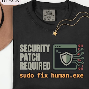 May include: A black t-shirt featuring the text SECURITY PATCH REQUIRED and sudo fix human.exe. The graphic includes a computer terminal window icon with a shield symbol and circuit lines. The shirt has a Comfort Colors brand label at the neck.